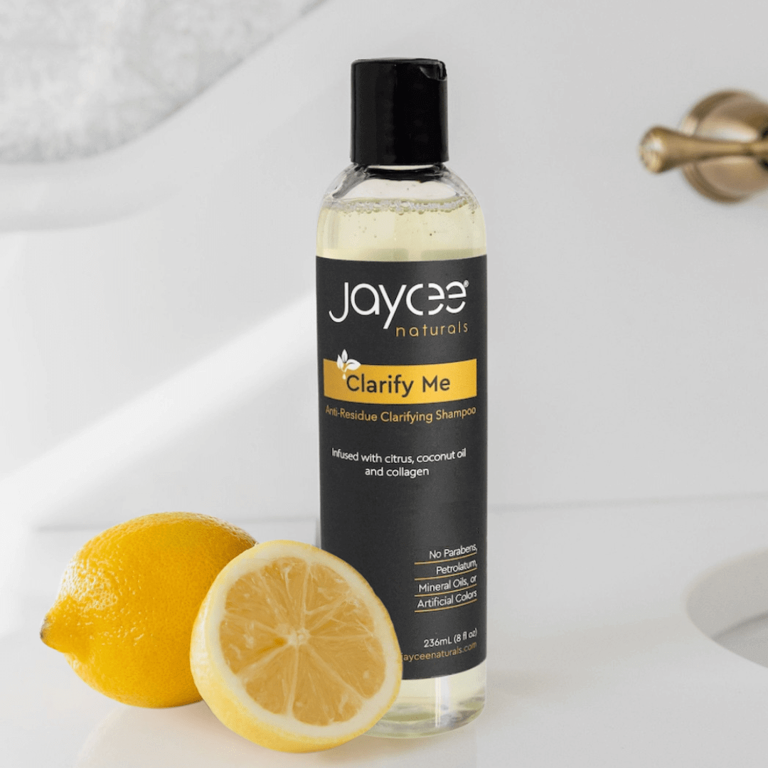 Jaycee Naturals Clarify Me Clarifying Shampoo, infused with citrus and coconut oil and free of parabens, petrolatum, mineral oils, and artificial colors. 236ml bottle standing on a white countertop and surrounded by lemons.