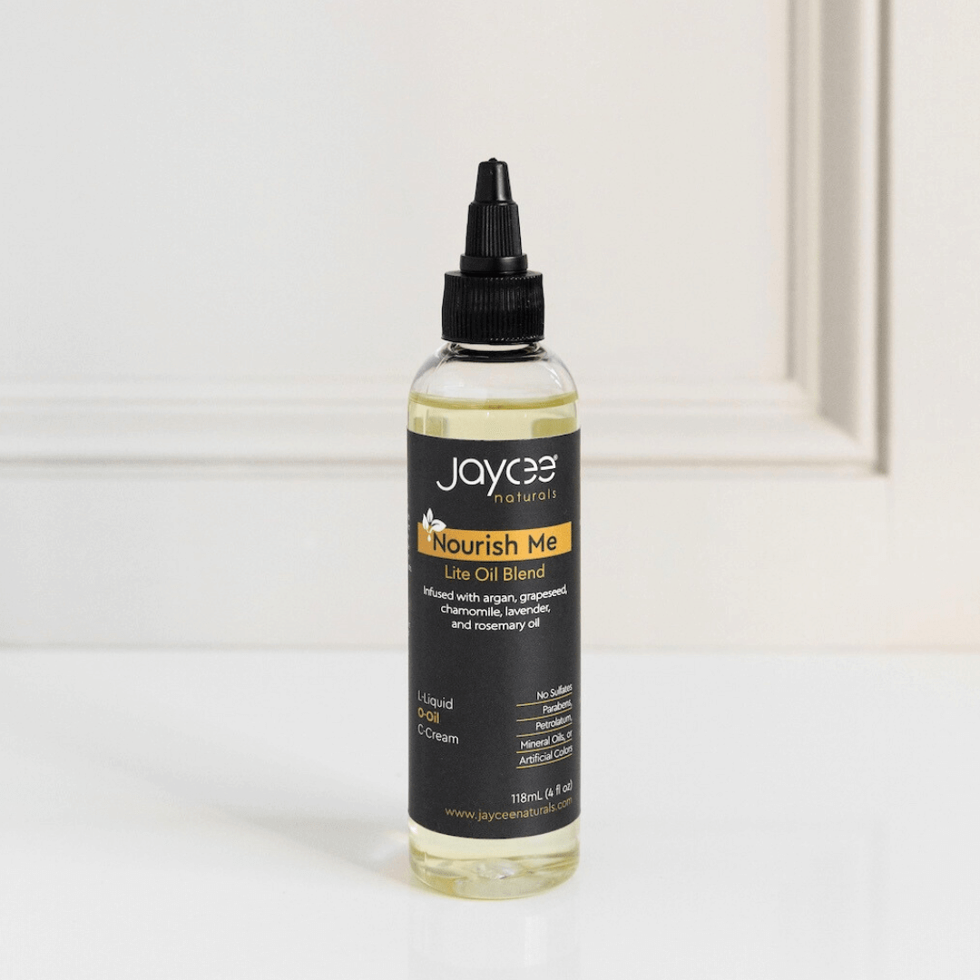 Jaycee Naturals Nourish Me Hair Oil, infused with argan and lavender oils, and free of sulfates, parabens, petrolatum, mineral oils, and artificial colors. 118ml bottle standing on a white countertop.