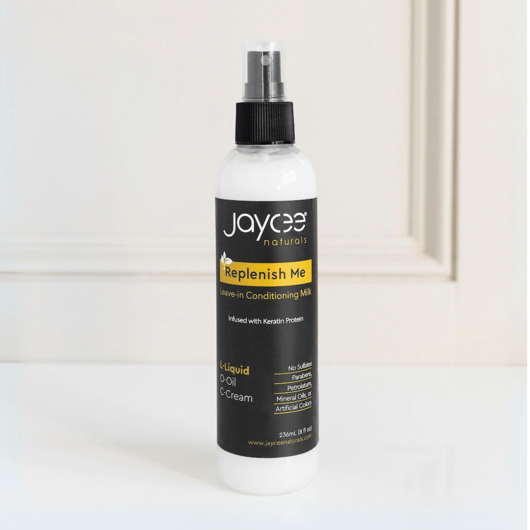 Jaycee Naturals Replenish Me Leave-In Conditioning Milk, infused with keratin protein and free of sulfates, parabens, petrolatum, mineral oils, and artificial colors. 236ml bottle standing on a white countertop.