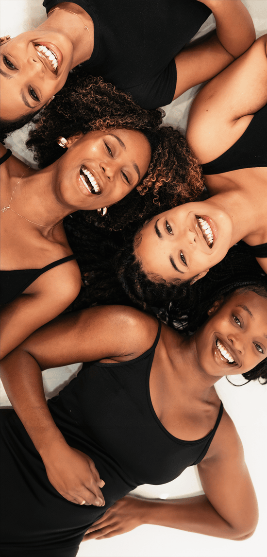 Four women laying together smiling on a plain background