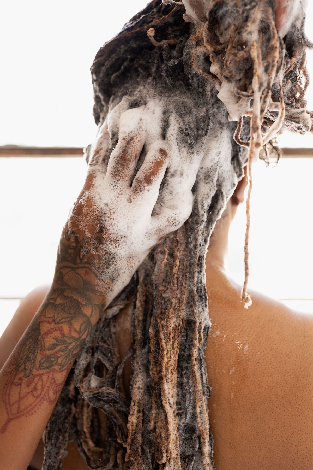 The back view of a woman with locs washing her hair