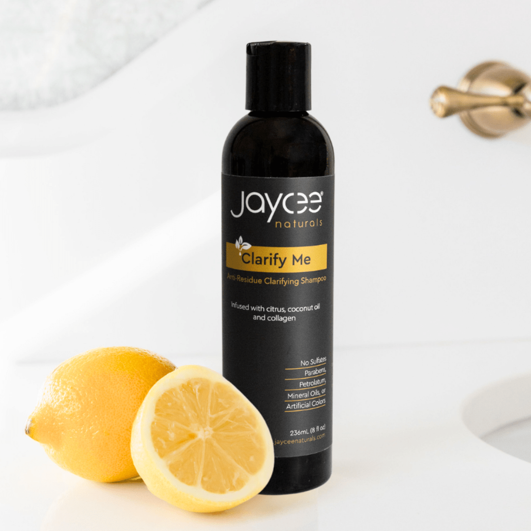 Jaycee Naturals Clarify Me Clarifying Shampoo, infused with citrus and coconut oil and free of sulfates, parabens, petrolatum, mineral oils, and artificial colors. 236ml bottle standing on a white countertop and surrounded by lemons.