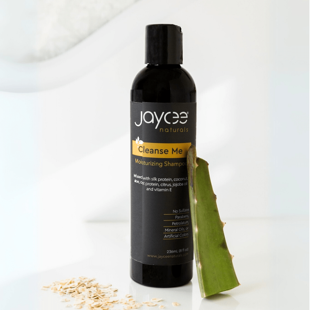 Jaycee Naturals Cleanse Me Moisturizing Shampoo, infused with silk protein and aloe and free of sulfates, parabens, petrolatum, mineral oils, and artificial colors. 236ml bottle standing on a white countertop and surrounded by oats and an aloe vera leaf.