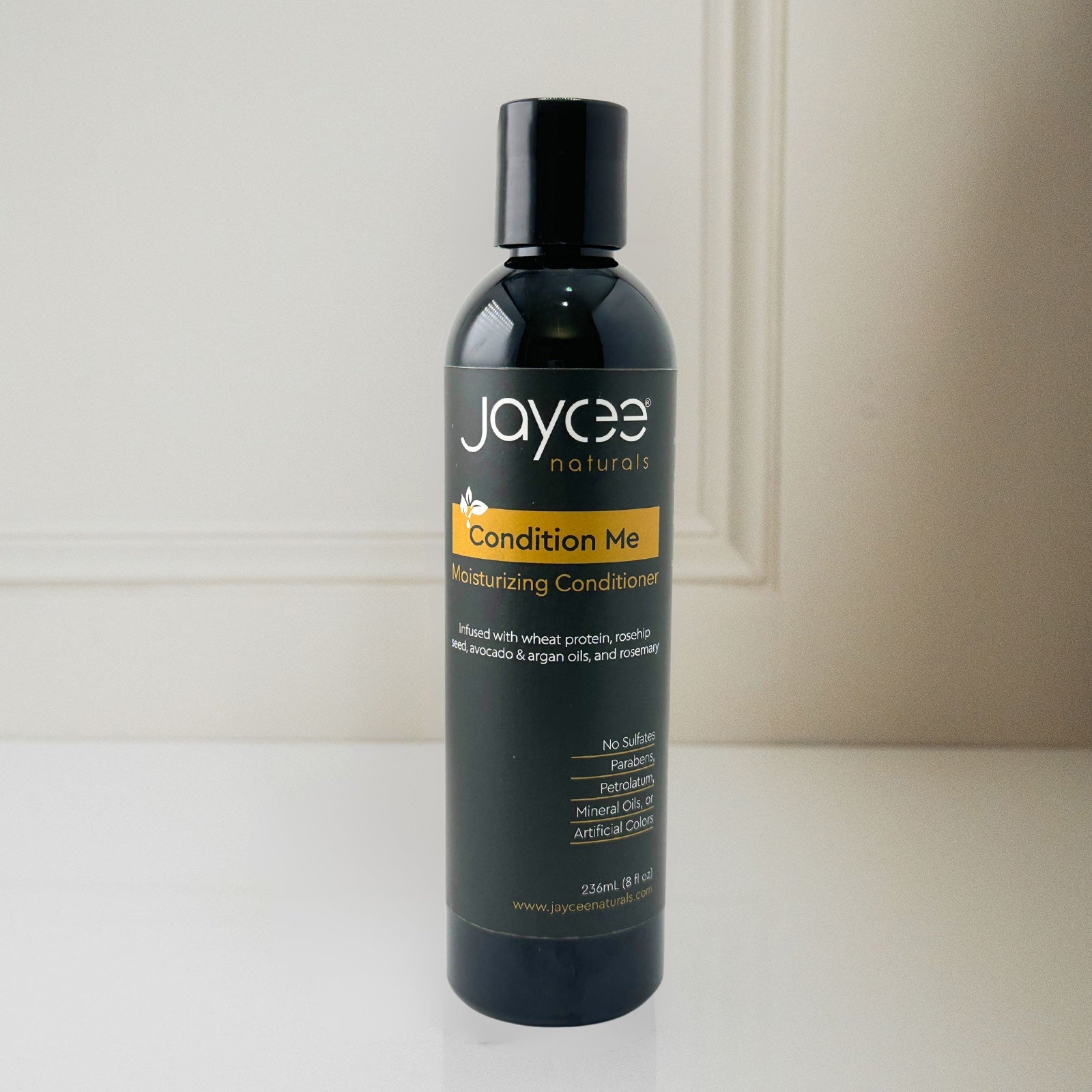 Jaycee Naturals Condition Me Moisturizing Conditioner, infused with wheat protein and free of sulfates, parabens, petrolatum, mineral oils, and artificial colors. 236ml bottle standing on a white countertop.