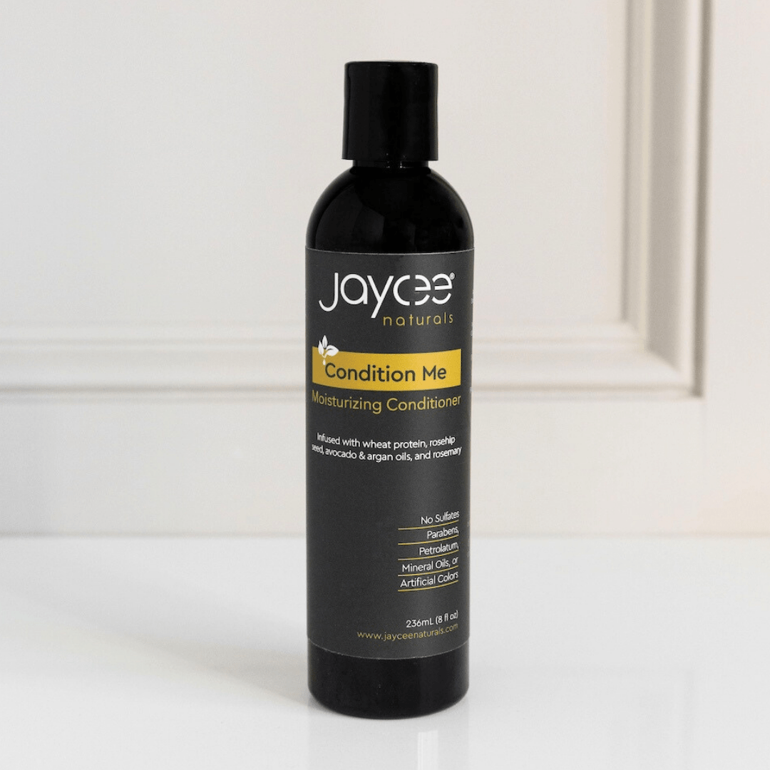 Jaycee Naturals Condition Me Moisturizing Conditioner, infused with wheat protein and argan oils and free of sulfates, parabens, petrolatum, mineral oils, and artificial colors. 236ml bottle standing on a white countertop.