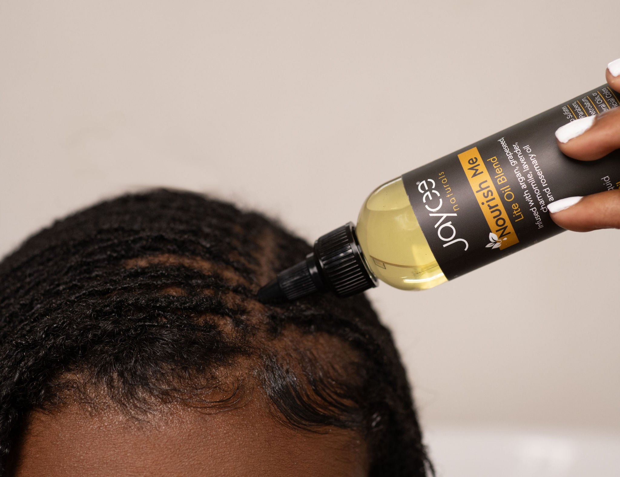 Person applying Nourish Me hair oil to locs and scalp against a neutral background