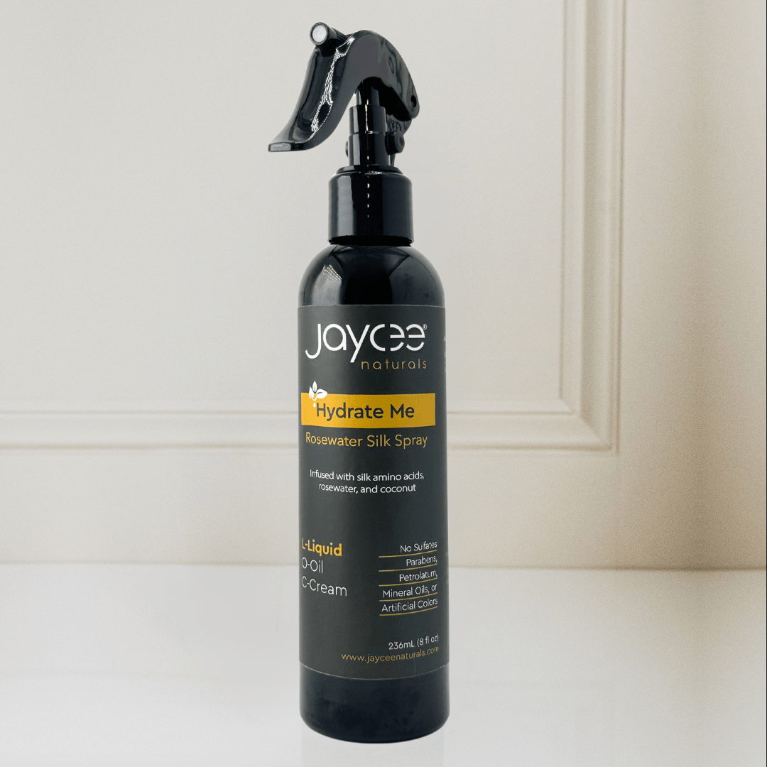 Jaycee Naturals Hydrate Me Rosewater Silk Spray, infused with coconut water and free of sulfates, parabens, petrolatum, mineral oils, and artificial colors. 236ml bottle standing on a white countertop.