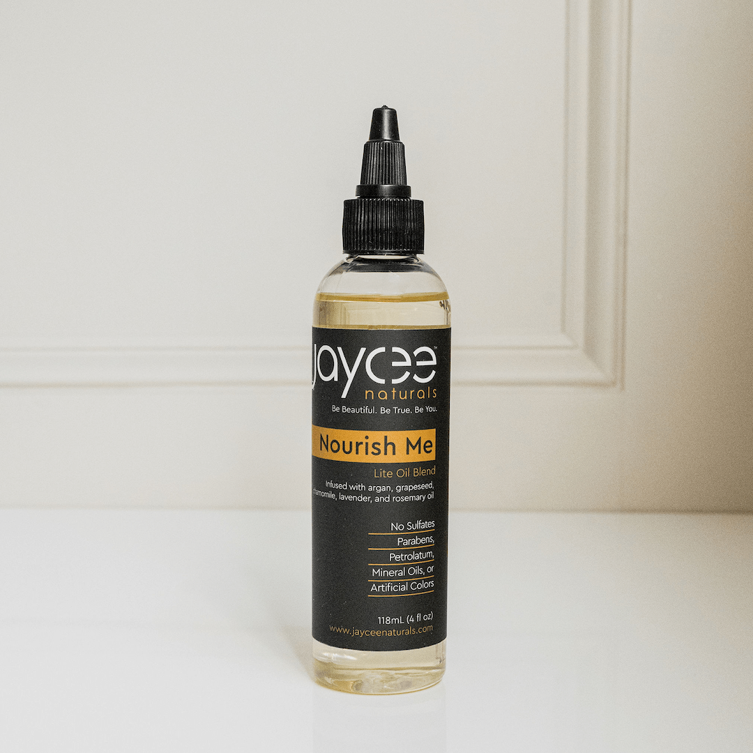 Jaycee Naturals Nourish Me Hair Oil, infused with essential oils and free of sulfates, parabens, petrolatum, mineral oils, and artificial colors. 118ml bottle standing on a white countertop.