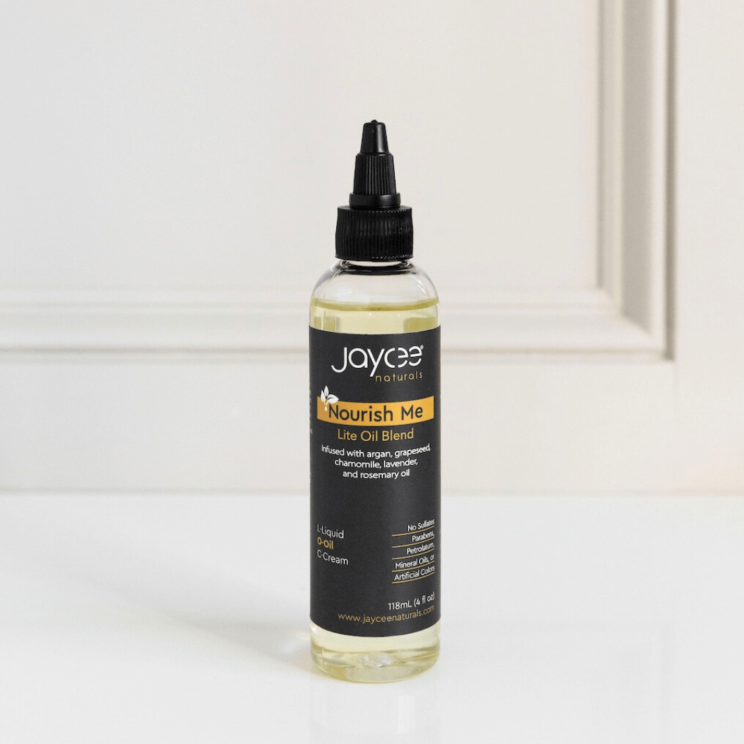 Jaycee Naturals Nourish Me Hair Oil, infused with argan and lavender oils, and free of sulfates, parabens, petrolatum, mineral oils, and artificial colors. 118ml bottle standing on a white countertop.