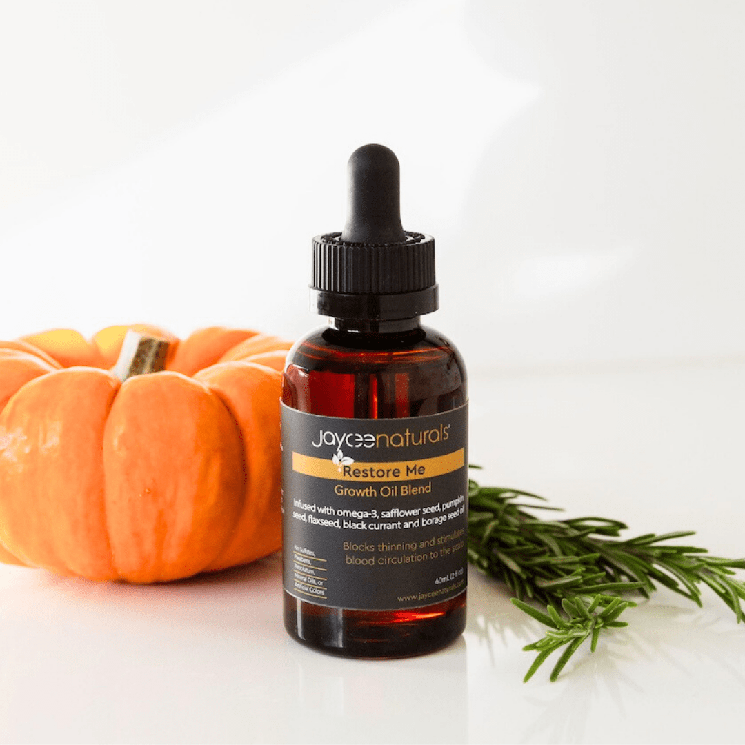 Jaycee Naturals Restore Me Growth Oil, infused with omega-3 and black currant oil, and free of sulfates, parabens, petrolatum, mineral oils, and artificial colors. 60ml bottle standing on a white countertop surrounded by a pumpkin and grapeseed.