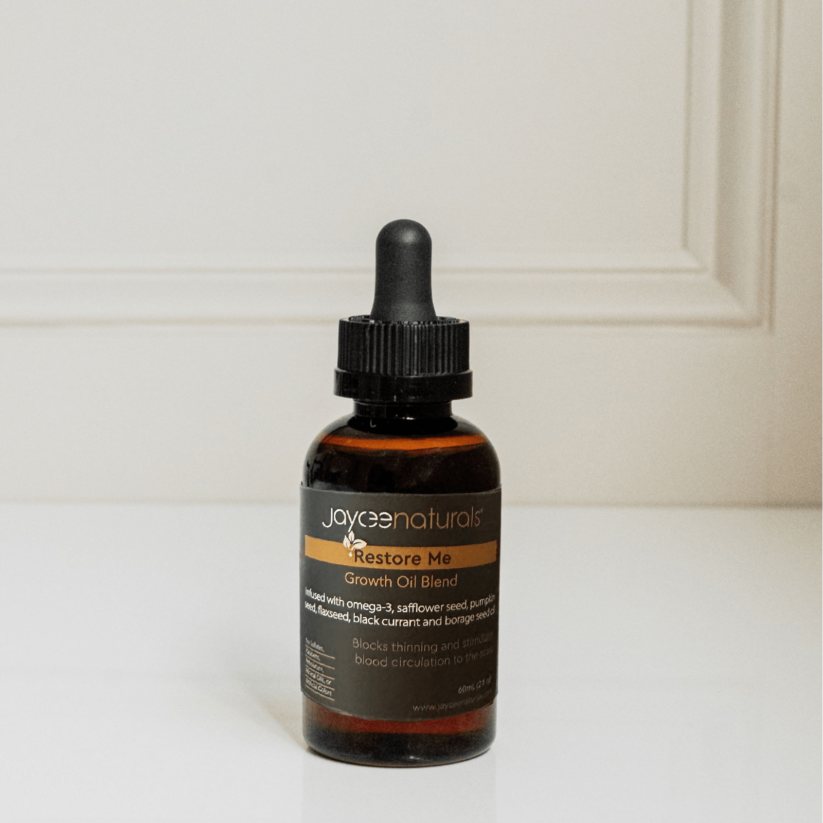 Jaycee Naturals Restore Me Oil Treatment, infused with essential oils and free of sulfates, parabens, petrolatum, mineral oils, and artificial colors. 60ml bottle standing on a white countertop.